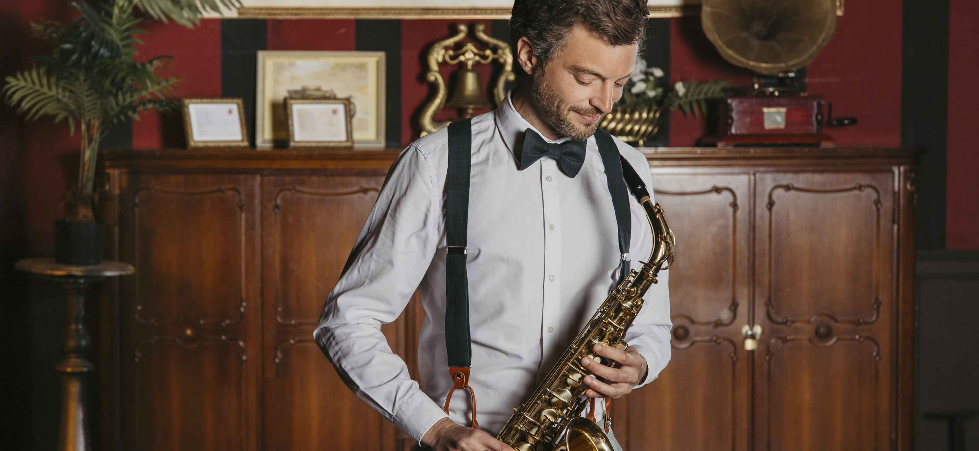 Herr mit Fliege und Hosenträger spielt Saxophon FAFIGO